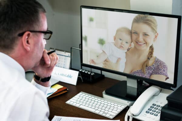 A healthcare professional engaging in a virtual consultation or a telemedicine appointment with a mother holding her baby, displayed on a computer monitor.