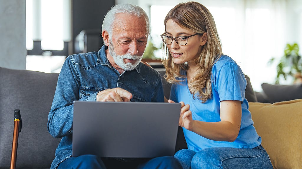 An elderly man and a healthcare worker looking at a laptop, possibly discussing medical terms for patient education.