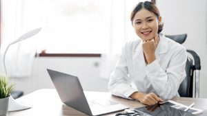 A medical professional sitting at a desk with a laptop, papers, and a friendly demeanor, ready to discuss post-diagnosis steps with a patient.