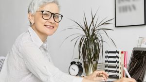 A professional woman with glasses smiling at her desk, representing the role of a 'Healthcare advocate.