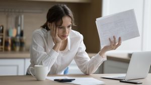 A woman appears confused while reading a medical document at her laptop, suggesting a challenge with health illiteracy.