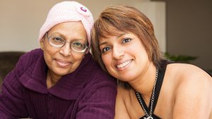 A warm, close-up image of two women, one with a headscarf, smiling at the camera, suggesting a moment of connection in long-distance caregiving.