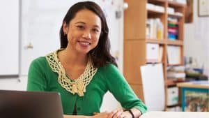 A healthcare professional at her desk with a laptop, smiling, which suggests she is involved in 'Customizing Care Plans' for patients.