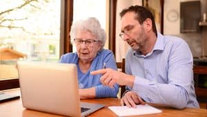 An elderly woman and a middle-aged man review health information on a laptop, indicating a collaborative approach to understanding healthcare.