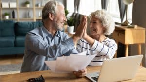 An elderly couple happily high-fiving each other over a set of medical documents, indicating a supportive moment in managing health care.