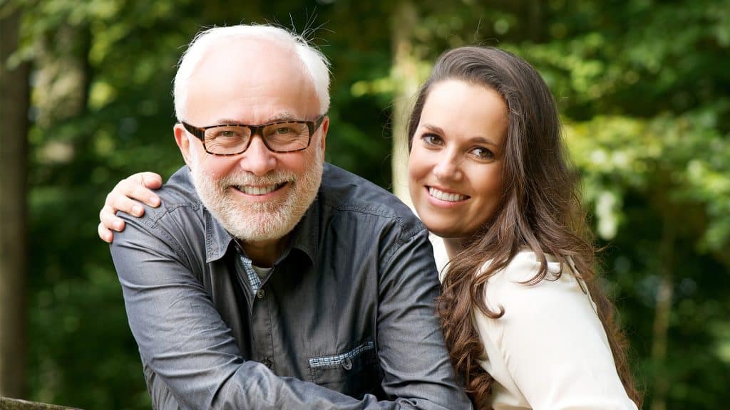 A smiling older man with glasses being embraced by a younger woman, possibly symbolizing positive 'progress notes' in a health or rehabilitation journey.