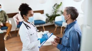 A healthcare professional wearing a mask taking notes while speaking with a patient, exemplifying 'Caseload Interactions' in a clinical setting.