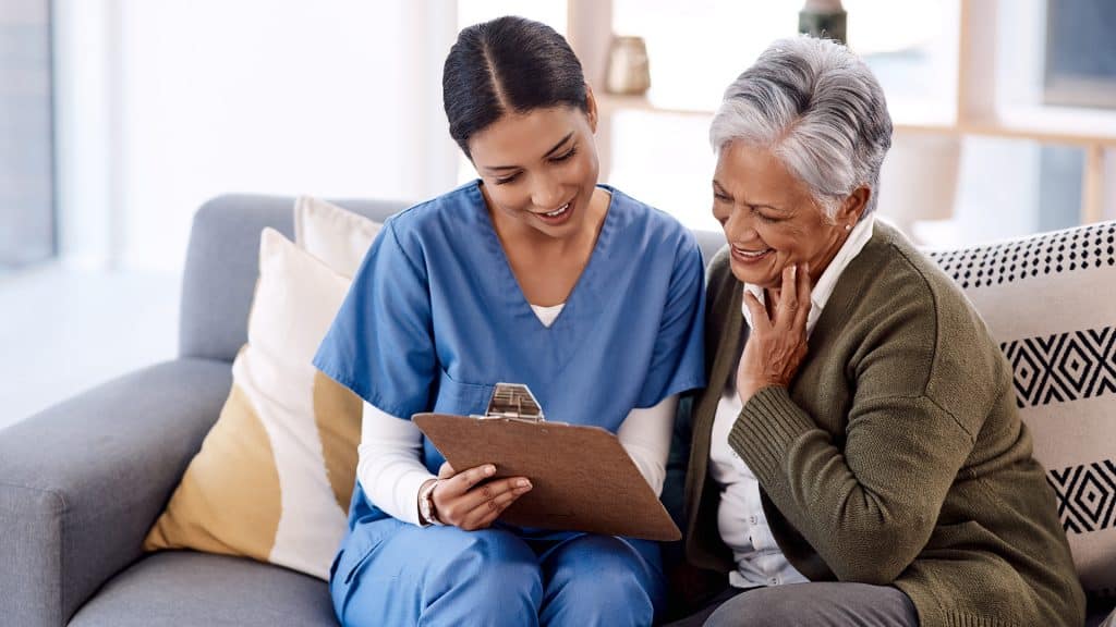 A nurse sitting beside an elderly woman, providing 'patient assistance' with healthcare information.