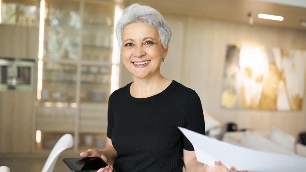 A smiling mature woman holding paperwork, possibly related to health literacy and self-management of her health care.