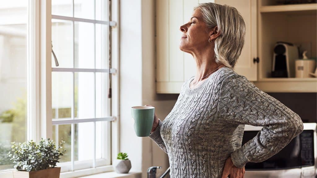 A contemplative woman holding a cup of coffee, possibly considering using a 'Drug Interaction Checker' to manage her medications.