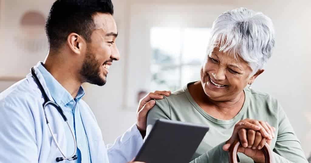 A healthcare worker and an elderly patient review information on a digital tablet, illustrating a respectful and professional interaction.