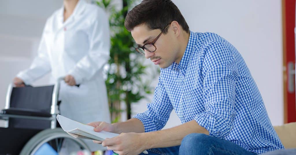 A man attentively filling out medical forms while a healthcare provider stands nearby, demonstrating 'self-responsibility' in managing personal health