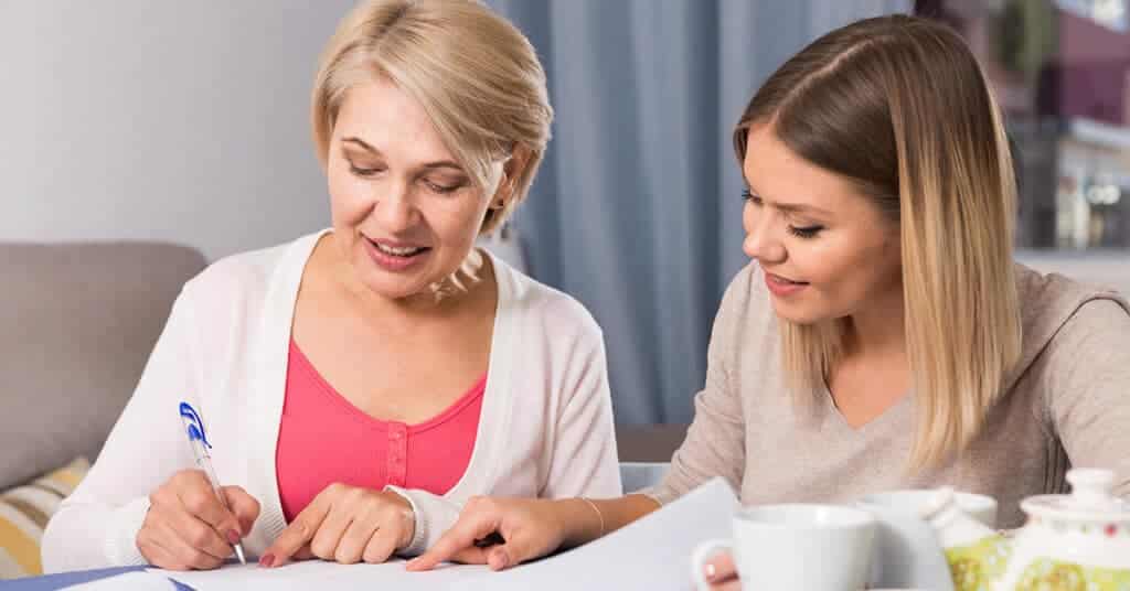 Two women reviewing documents together, with one explaining to the other, embodying 'Clear Communication' in understanding healthcare information.