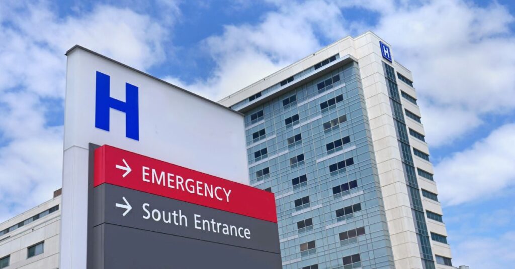 A modern hospital building with a large "H" sign in the foreground indicating the healthcare facility. The sign directs visitors to the emergency department and the south entrance, emphasizing accessibility and navigation within the healthcare system. The building features sleek, glass-paneled architecture under a clear blue sky, symbolizing the advanced infrastructure and professionalism of the healthcare industry.