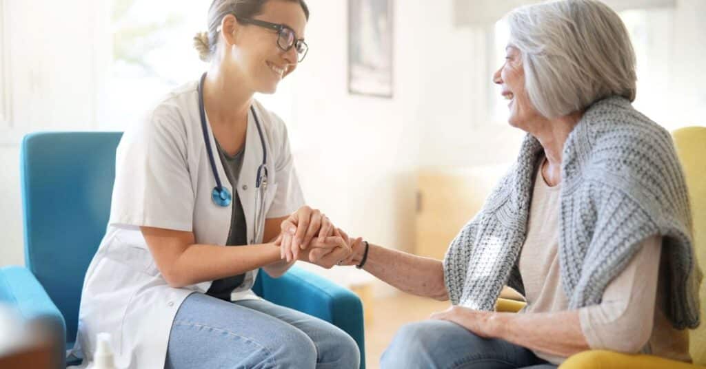 A compassionate healthcare provider engaging with an elderly patient in a cozy home setting, symbolizing the essence of home healthcare. The provider's warm smile and attentive demeanor reflect personalized care, emphasizing the importance of delivering quality medical support and companionship directly in the patient's home environment.