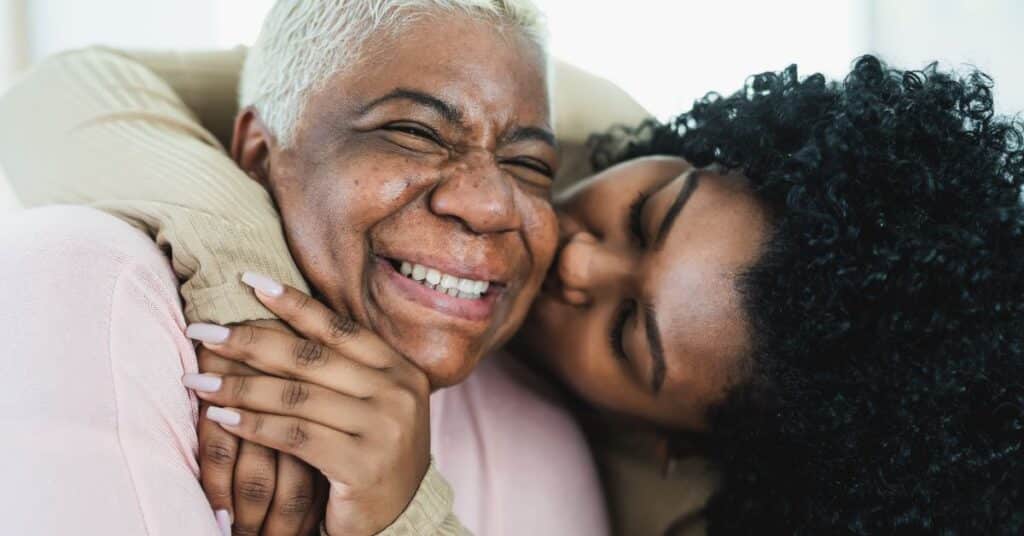 A joyful moment between an elderly woman and her adult daughter, showcasing the loving bond and support provided by informal caregivers. The adult daughter embraces her mother warmly, symbolizing the essential role of informal caregivers in providing emotional and practical assistance in daily life, often without professional training or formal recognition.