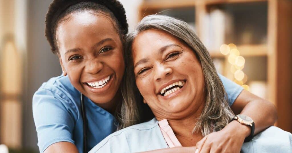 This image depicts a smiling caregiver embraces a happy elderly woman, symbolizing the compassion and support provided in caregiving.
