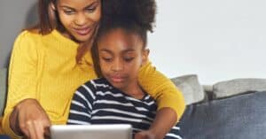 A mother and daughter sitting on a couch, both looking at a tablet together, exemplifying the importance of advanced planning and scheduling in managing healthcare efficiently.