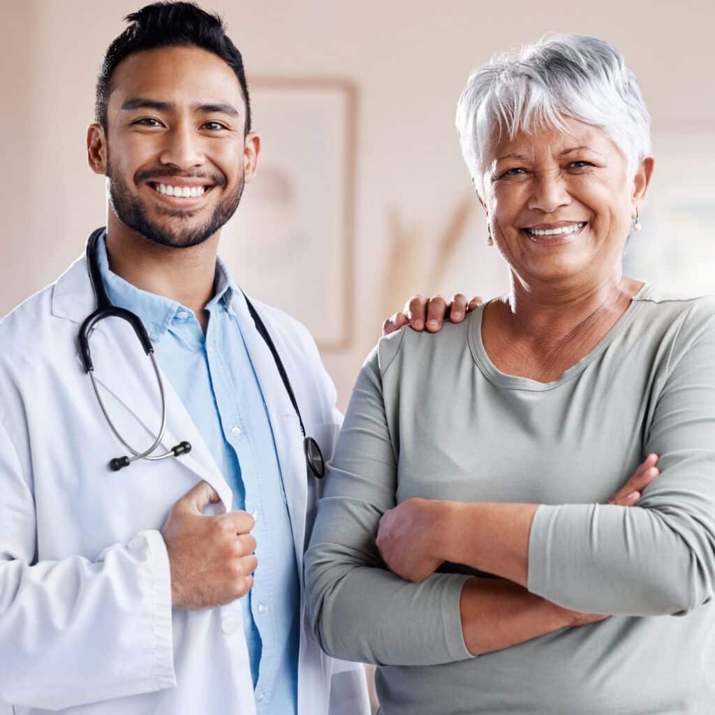 A smiling doctor standing beside an elderly woman, both appearing confident and content. The doctor has his arm around the woman's shoulder, reflecting a positive and supportive healthcare relationship.