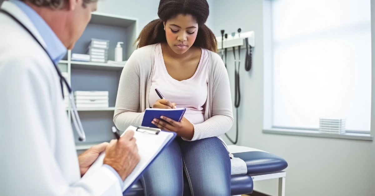 A young patient is seated on an exam table in a doctor's office, attentively writing in a blue notebook while a physician, who is also holding a clipboard, observes her. The image emphasizes the importance of bringing a notebook to medical appointments for effective communication and record-keeping.
