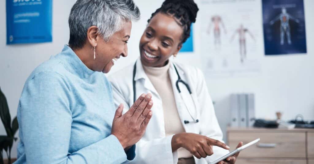A healthcare provider discusses a DME order with a smiling patient in a clinic setting, showing the collaborative process of managing healthcare needs using a digital tablet.