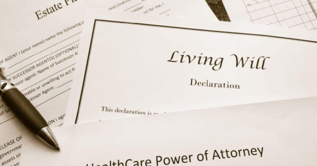 A close-up image of various legal documents related to advance directives, including a "Living Will Declaration" and a "Healthcare Power of Attorney." A pen is placed beside the documents, suggesting readiness for review or signature. The papers emphasize the importance of end-of-life planning and decision-making authority for healthcare.