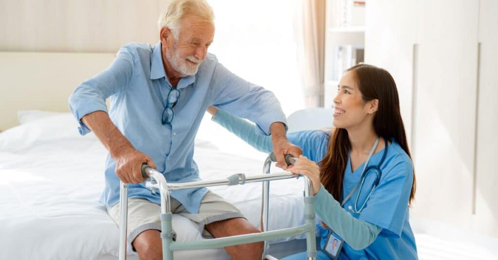 A healthcare professional in blue scrubs is gently assisting an elderly patient using a walker in a bright, well-lit room, illustrating the concept of Continuity of Care by showcasing ongoing, compassionate support and coordination in a home or clinical setting.