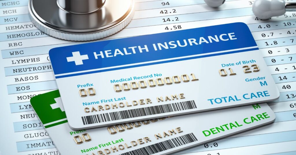 A stack of health insurance cards labeled for medical, dental, and total care services, placed on top of medical records and a stethoscope.