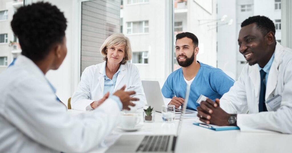 A diverse group of medical professionals, including doctors and researchers, sits around a conference table in a bright, modern office, engaged in a discussion. Laptops, notebooks, and documents are spread across the table, symbolizing collaboration and the rigorous evaluation process involved in peer-reviewed research. The attentive expressions and professional setting highlight the importance of experts reviewing studies for accuracy, validity, and adherence to scientific standards before publication.