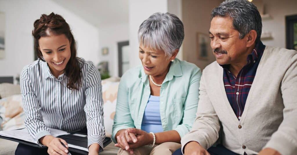 A friendly healthcare professional provides care navigation support to an older couple, reviewing documents and explaining their healthcare options together.