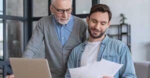 Two men reviewing healthcare documents on HEDIS vs CAHPS surveys, discussing differences in quality measurement and patient experience.