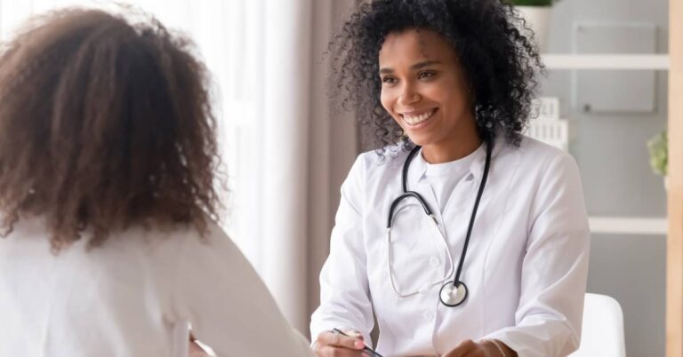 A primary care doctor smiling while talking with a patient during a check-up, representing compassionate and continuous healthcare support.