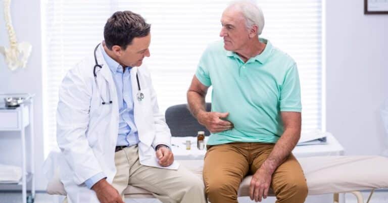 An older man describing abdominal pain to his doctor during a medical visit, illustrating how patients communicate symptoms to identify possible health concerns.