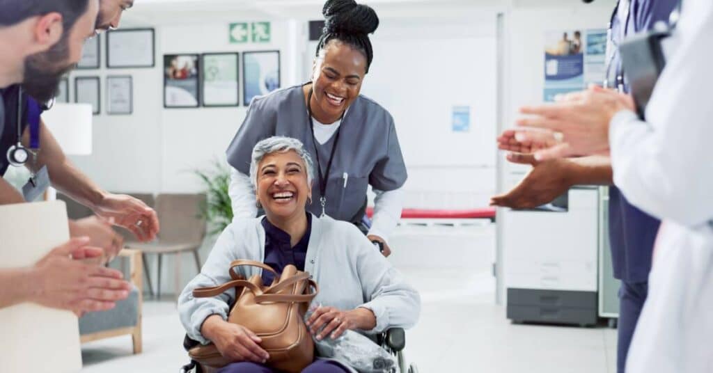 A smiling patient in a wheelchair being applauded by healthcare staff, celebrating recovery milestones and progress toward personal and therapeutic goals.