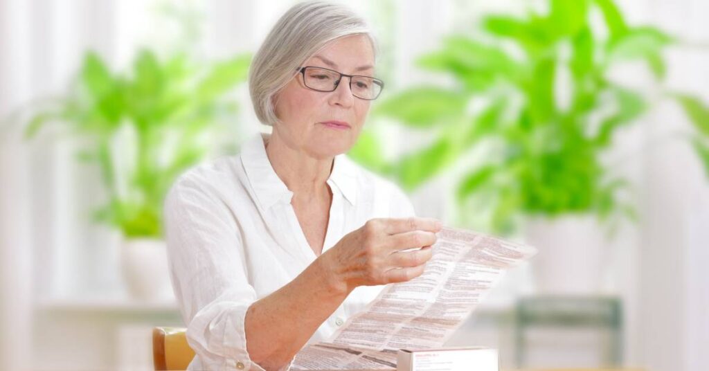An older woman reading a package insert carefully to understand her medication’s directions, side effects, and safety information at home.