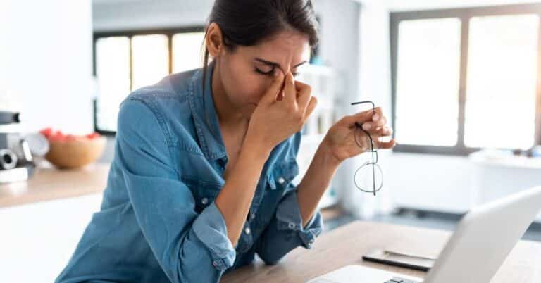 A woman experiencing discomfort and holding her head in pain at home, illustrating a possible adverse event related to medication or treatment.