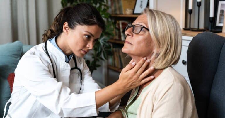 A doctor gently examining a woman’s neck for thyroid issues during a consultation, representing endocrinology and hormone-related healthcare