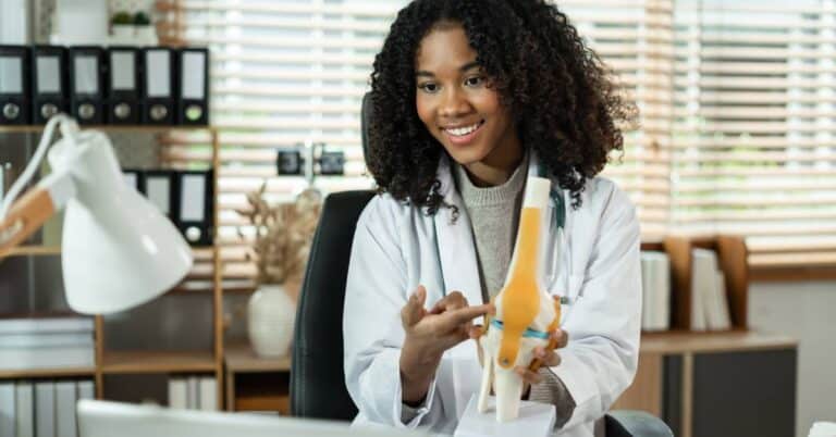 A smiling orthopedic doctor explains a knee joint model to a patient, demonstrating how orthopedics helps diagnose and treat bone and joint conditions.