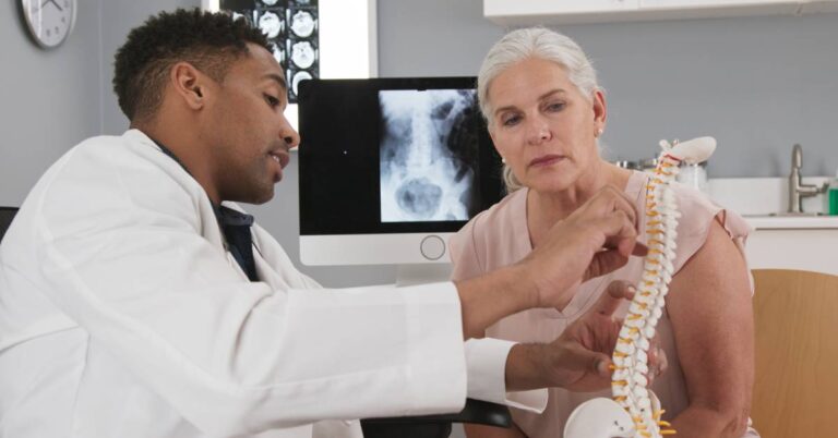 A pain management specialist explaining spine anatomy and treatment options to a patient using a model and X-ray, illustrating diagnosis and personalized pain relief care.