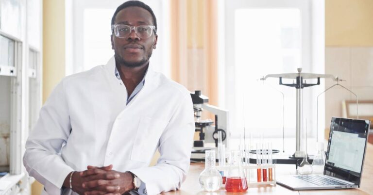 A pathologist in a laboratory surrounded by test tubes, microscope, and laptop, representing pathology, disease diagnosis, and medical laboratory analysis.