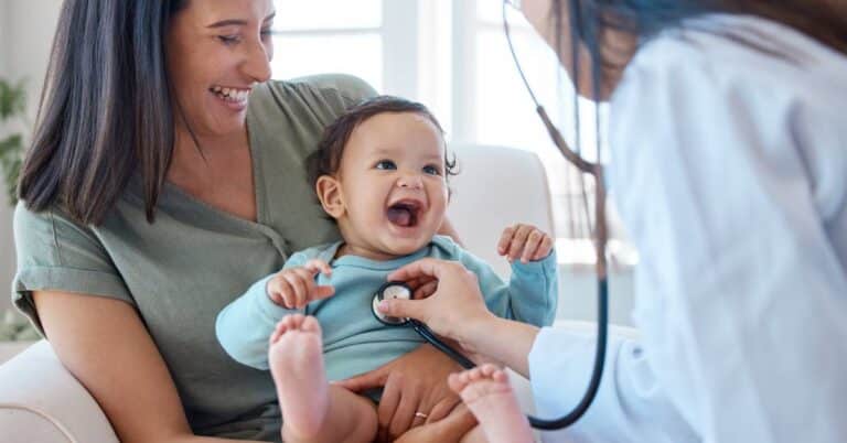 A pediatrician uses a stethoscope to check a smiling baby during a pediatrics appointment, highlighting compassionate child health and family-centered care.
