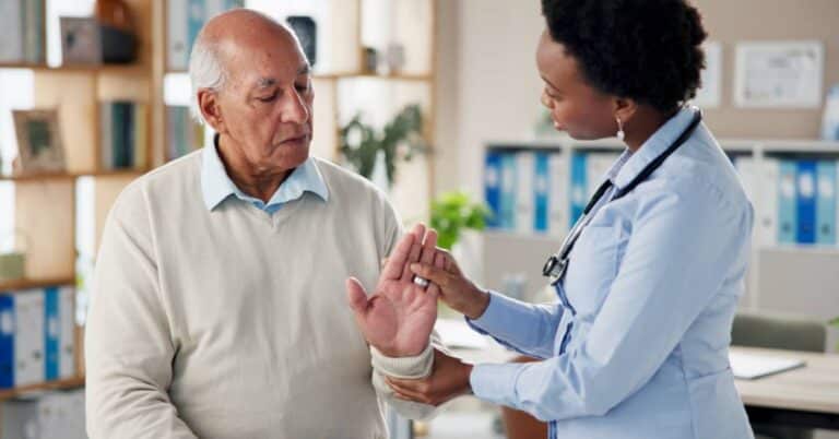 A plastic surgeon examining an older patient’s hand in a medical office, illustrating how plastic surgery restores function and improves quality of life.