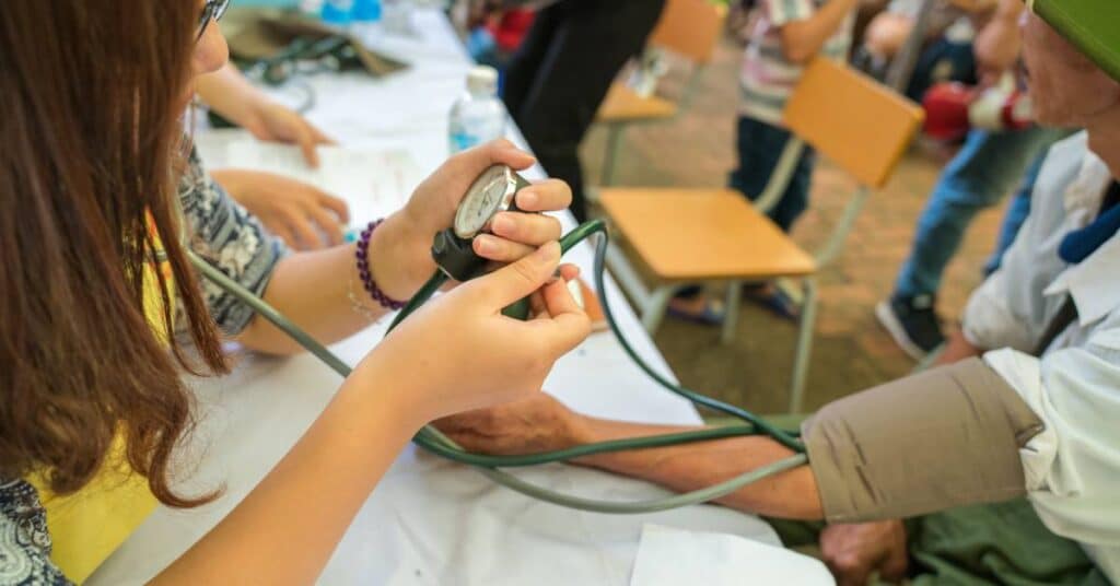A healthcare worker checking an elderly person’s blood pressure during a community health event, representing hands-on crisis care management and patient support in urgent care situations.