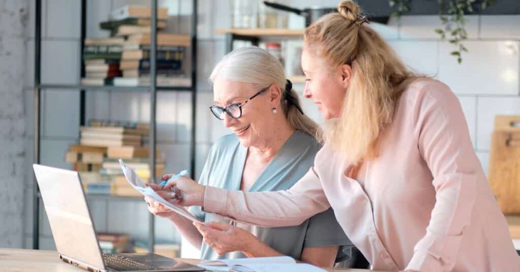 Two women reviewing documents together at a laptop, representing Patient Better’s health management resources that help people organize and understand their care.
