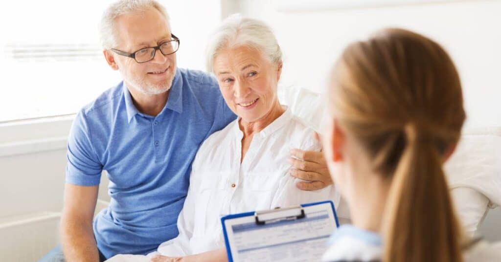 An older woman acting as a healthcare proxy supports a couple during a medical consultation, helping them improve their navigation skills and coordinate their care.