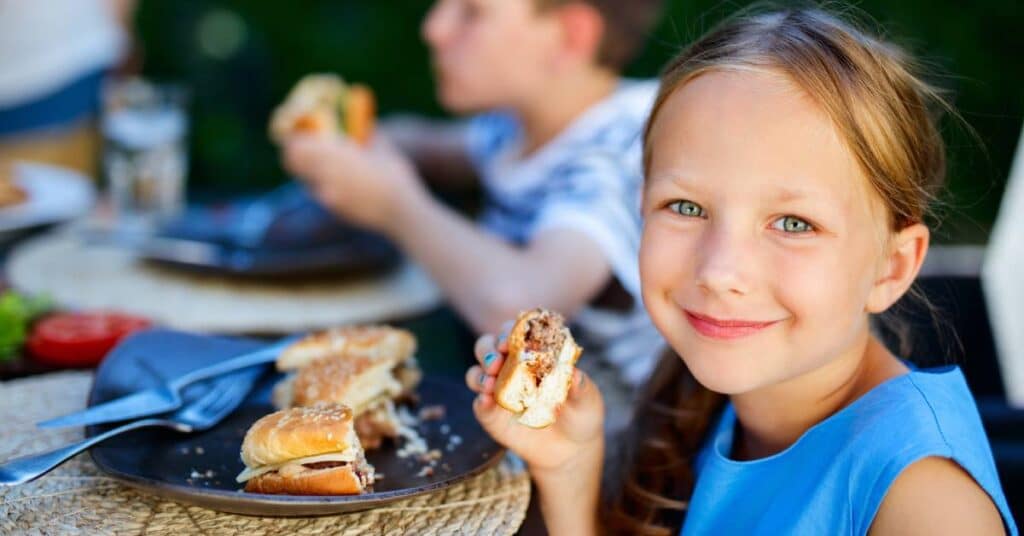 Children eating burgers outdoors.