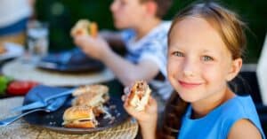 Children eating burgers outdoors.
