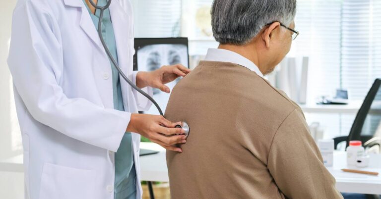 A doctor uses a stethoscope to listen to an older patient’s back during a check-up in a medical office, representing a healthcare service that would be documented using the Current Procedural Terminology (CPT) code system for accurate billing and insurance claims.