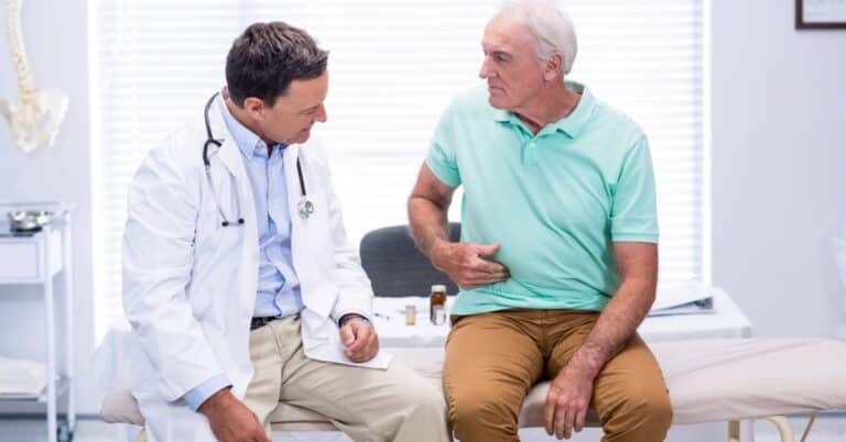 A doctor listens to an older male patient describing abdominal pain during a consultation, representing how healthcare professionals use the International Classification of Diseases (ICD) system to document and code medical symptoms and diagnoses accurately.