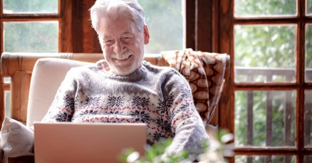 Older man smiling while video chatting with his family on a laptop, illustrating long-distance caregiving and staying connected with loved ones from afar.